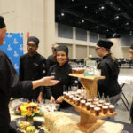 Several culinary arts students have a discussion in front of prepared dishes