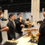 Several culinary arts students have a discussion in front of prepared desserts