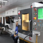 Two individuals sit inside of the mobile manufacturing training lab trailer next to equipment
