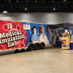A large trailer on the show floor containing a medical simulation lab