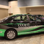 A car situated on the show floor, wrapped in decals promoting an Automotive Systems Technology program