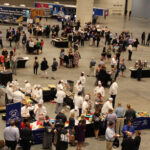 A high-elevation photo of the show floor with several dozen participants