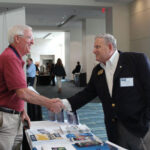 A participant and a representative shake hands across an information table